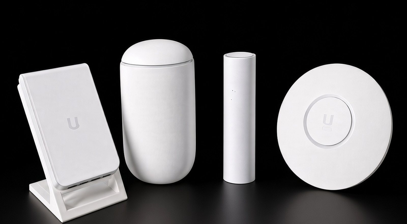 Studio shot of four white UniFi-style devices on black: an in-wall access point on a small stand, a Dream Router cylinder, a slim U6 Mesh access point, and a round access point
